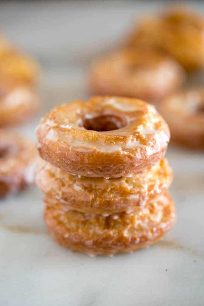 Three homemade sour cream donuts stacked on top of each other with more donuts in the background.