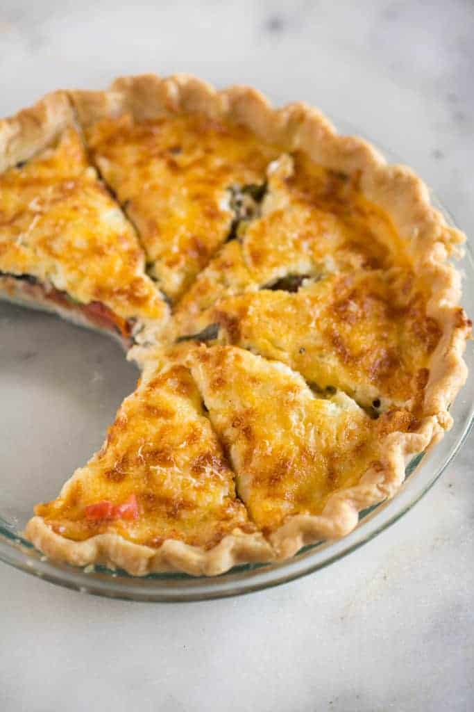 A clear glass pie pan filled with a baked tomato pie cut into slices, with two pieces removed.