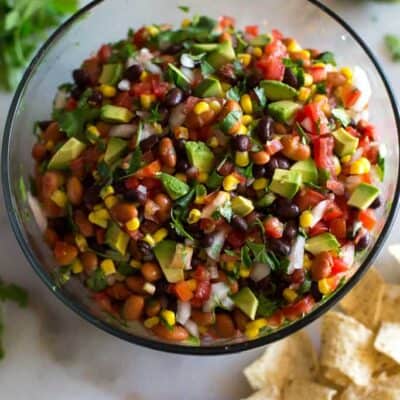 Cowboy Caviar served in a big glass bowl with chips, cilantro and a halved lime on the sides.