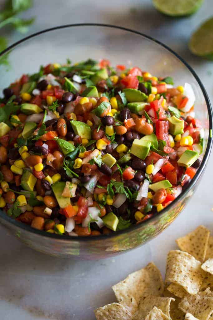 Black beans, pinto beans, corn, diced tomato, avocado, cilantro and onion mixed and served in a bowl with chips on the side.