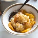 Peach cobbler served in a bowl with a spoon, and another bowl of cobbler in the background.