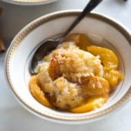 Peach cobbler served in a bowl with a spoon, and another bowl of cobbler in the background.