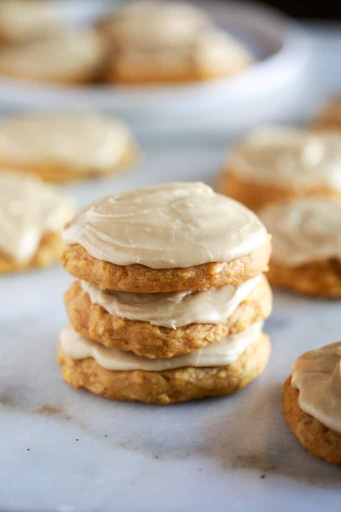 A stack of three pumpkin cookies, with more cookies in the background.