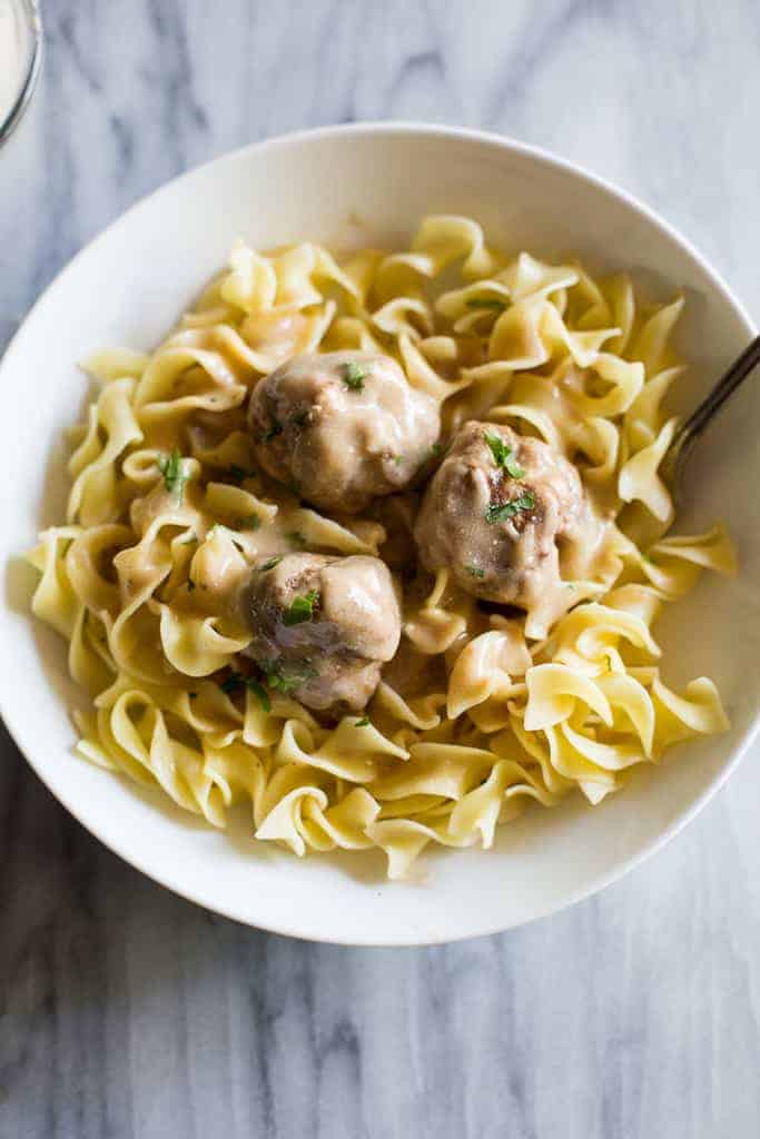 Three Swedish Meatballs and gravy served over egg noodles in a white bowl with a fork.