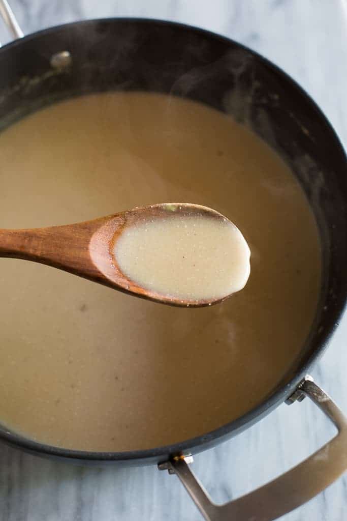 A spoonful of gravy being lifted from a pan with a wooden spoon. 
