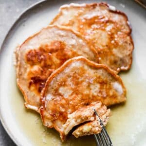 Three apple pancakes on a plate with a fork taking a bite.