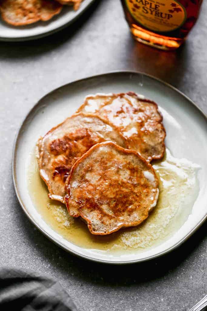 Three Apple Pancakes overlapping on a plate with syrup on top.