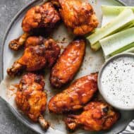 Baked chicken wings in buffalo sauce on a plate with a side of ranch and celery.