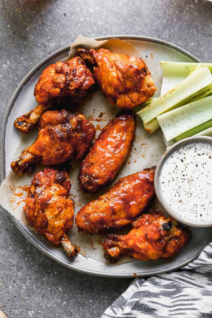 Baked chicken wings in buffalo sauce on a plate with a side of ranch and celery.