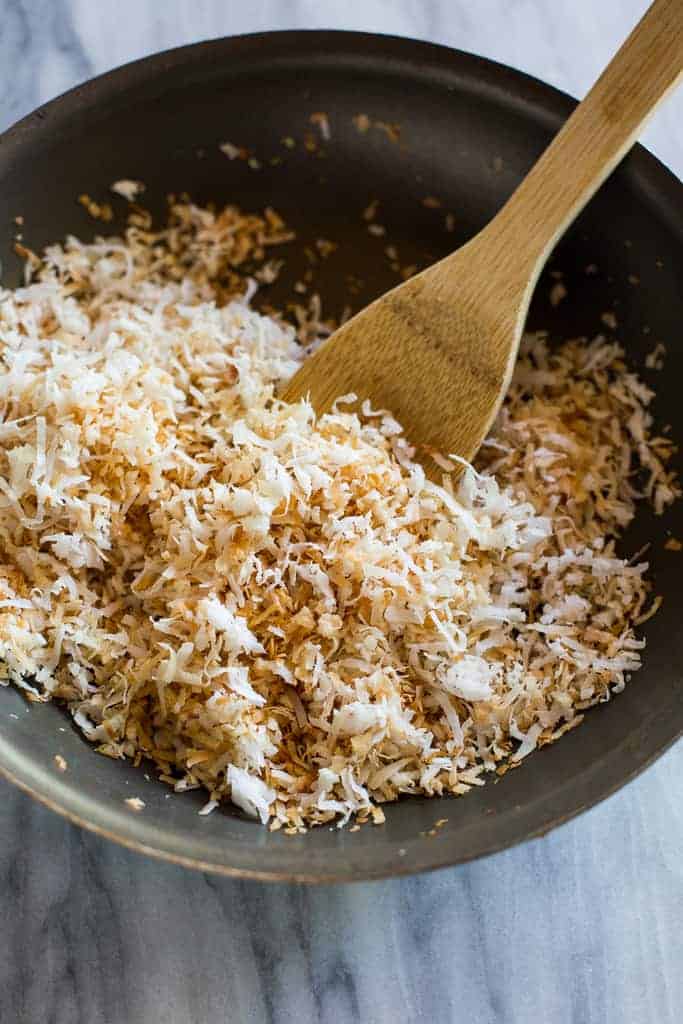 Overhead photo of a skillet with toasted coconut and a wooden spoon.