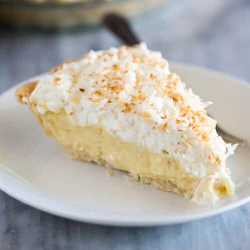 A slice of coconut cream pie on a white plate with a fork.