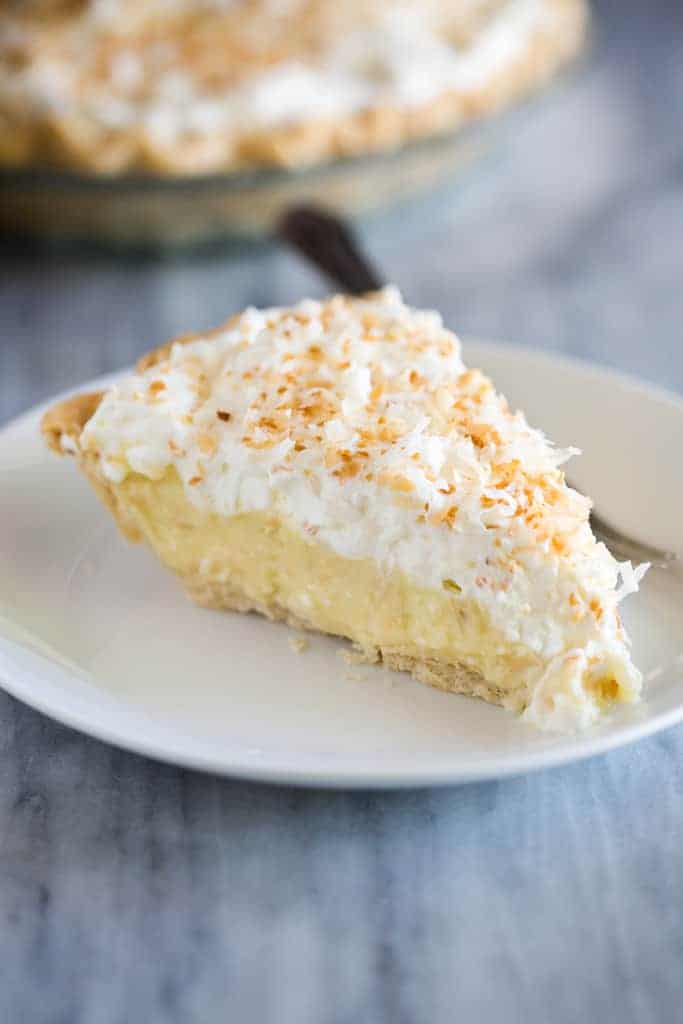 A slice of coconut cream pie on a white plate with a fork.