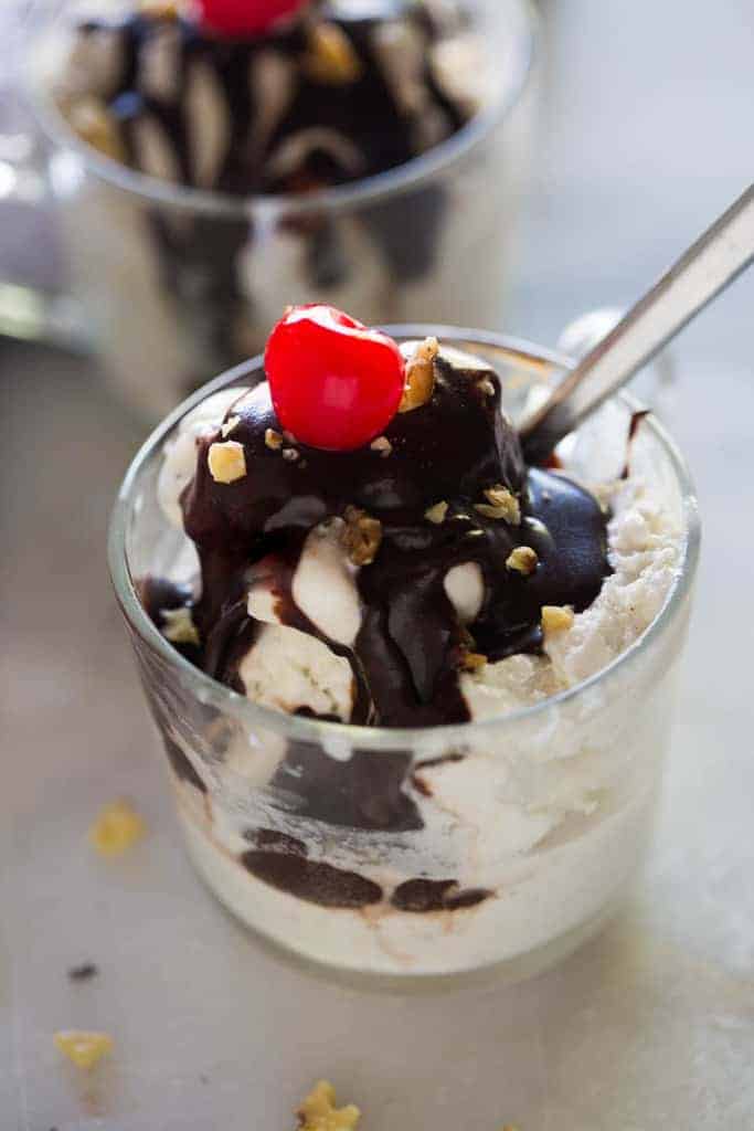 A cup full of vanilla ice cream with hot fudge, walnuts and a cherry on top.