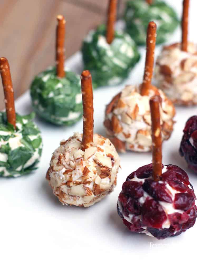 Mini Cheese Ball Bites that are rolled in various toppings with a pretzel sticking out of them.