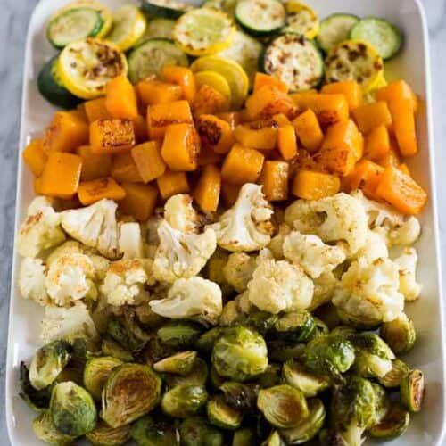 Roasted Vegetables on a white tray including butternut squash, brussels sprouts, cauliflower, and zucchini.