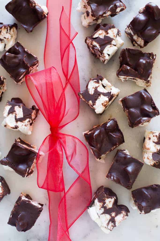 A white marble board with square pieces of rocky road chocolate and marshmallow fudge with a red ribbon 