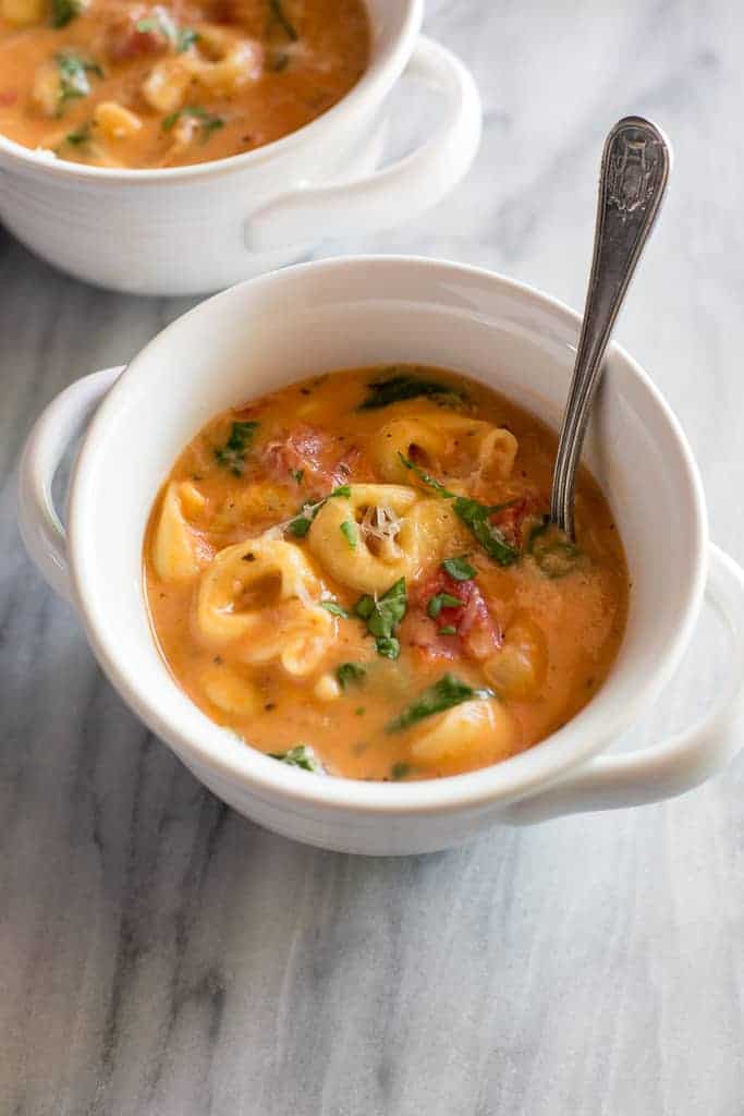 Tortellini Soup with spinach and tomatoes in it in a white bowl with a spoon.