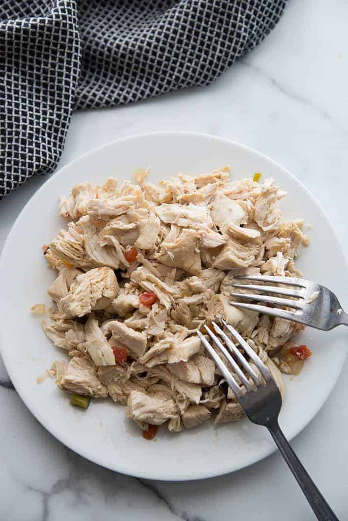 A plate full of shredded chicken with two fork resting on it.