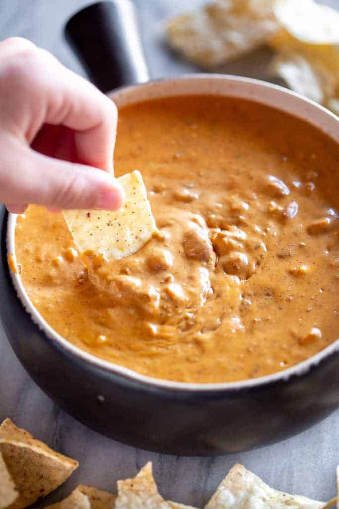 A hand dipping a tortilla chip in chili cheese dip.
