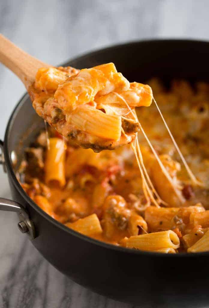 Baked Ziti made in a skillet with ziti noodles, cheese and sausage, with a wooden spoon scooping out a serving.