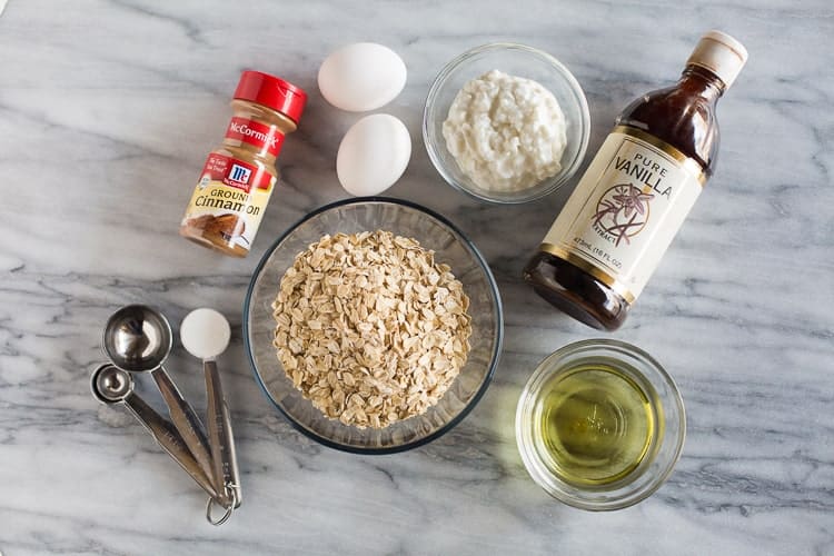 Overhead photo of the ingredients for protein pancakes, including a bowl of oats, olive oil and water, two eggs, cottage cheese, cinnamon, baking powder and vanilla.