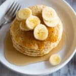 Protein Pancakes served with sliced bananas and syrup on a white plate with a fork.