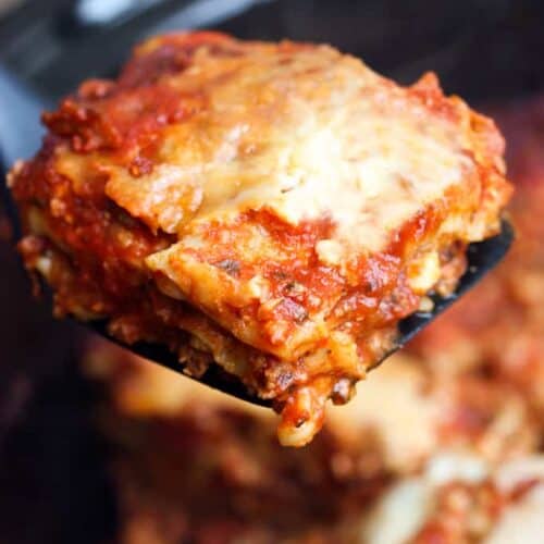 A slice of slow cooker lasagna being lifted from the crock pot.
