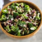Broccoli salad with bacon, craisins, almonds and a creamy dressing, served in a wooden bowl with a hand towel in the background.