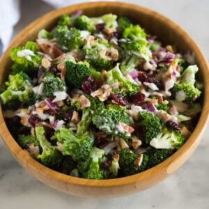 Broccoli salad with bacon, craisins, almonds and a creamy dressing, served in a wooden bowl with a hand towel in the background.