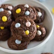 Chocolate cookies with mini cadburry egg pieces, on a white plate.