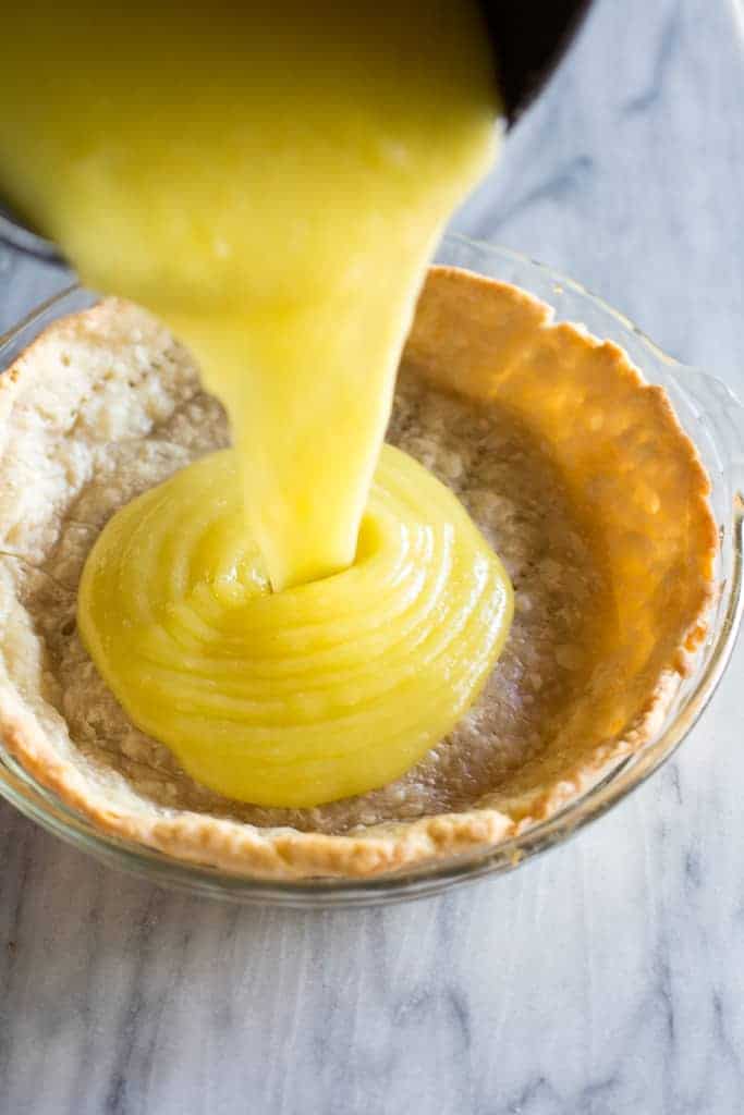 Lemon pie filling being poured into a pie shell to make lemon meringue pie.