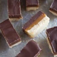 Homemade twix bars with layers of shortbread, caramel and chocolate, cut into rectangles, placed on a grey board.