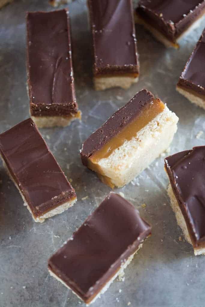 Homemade twix bars with layers of shortbread, caramel and chocolate, cut into rectangles, placed on a grey board.