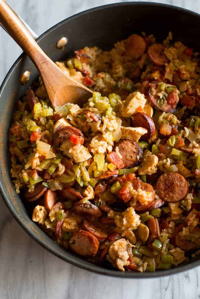 Overhead photo of a large skillet filled with Jambalaya, including rice, chicken and sausage, with a wooden spoon in the skillet for serving.