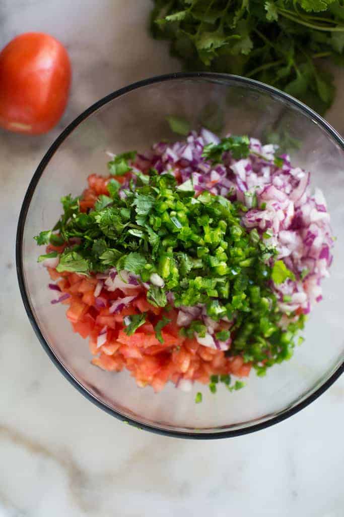 A bowl with the ingredients for pico de gallo including diced tomato, onion, cilantro, and jalepeno.