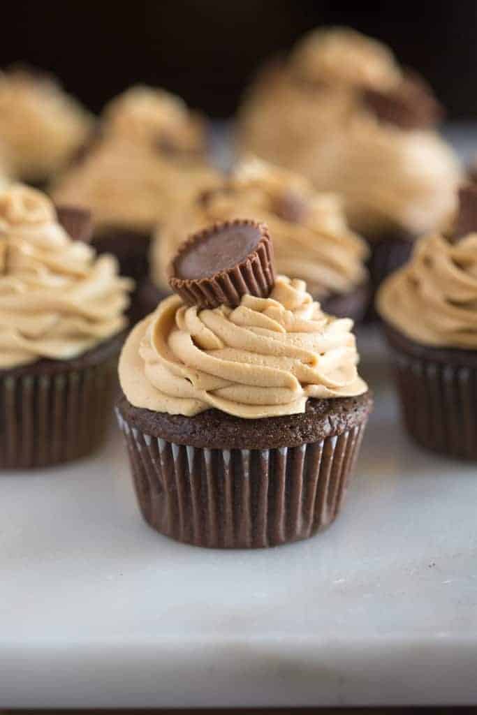 Chocolate cupcakes with peanut butter frosting and a mini Reese's peanut butter cup placed on top, served on a white marble board.