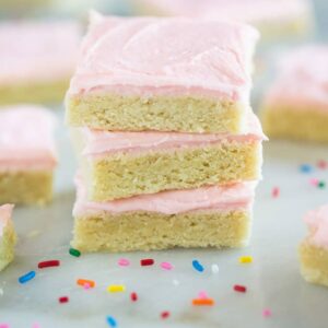 A stack of sugar cookie bars with pink frosting, on a marble board with sprinkles.