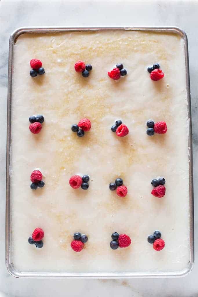 Overhead photo of almond sheet cake baked in a jelly roll pan and topped with raspberries and blueberries.