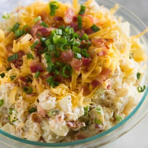 A bowl full of baked potato salad including chopped potatoes, bacon, green onions and shredded cheese.