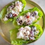 Three lettuce cups on a plate filled with chicken salad mixture with cut grapes and apples in it.