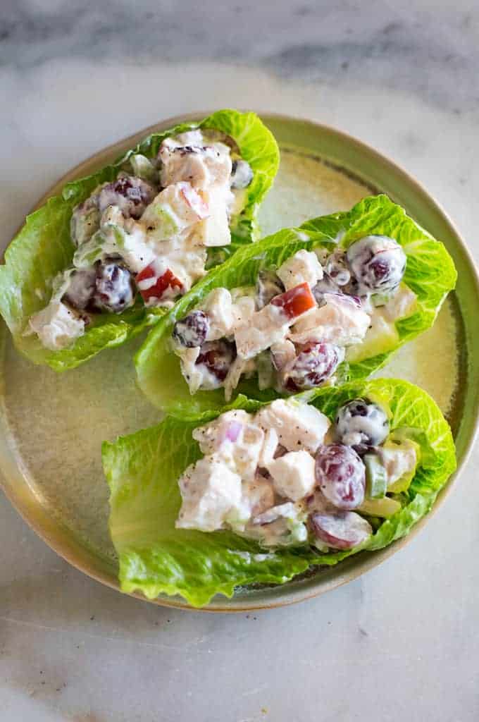 Three lettuce cups on a plate filled with chicken salad mixture with cut grapes and apples in it.