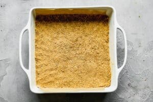 Homemade graham cracker crust pressed into a square baking pan.