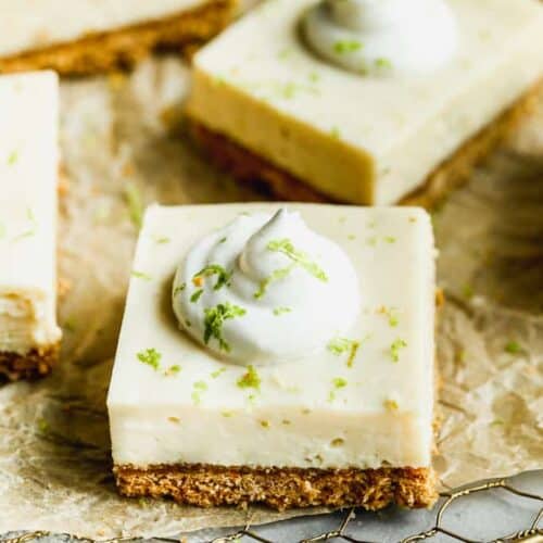 Key lime pie bars with whipped cream on top and garnished with lime zest.