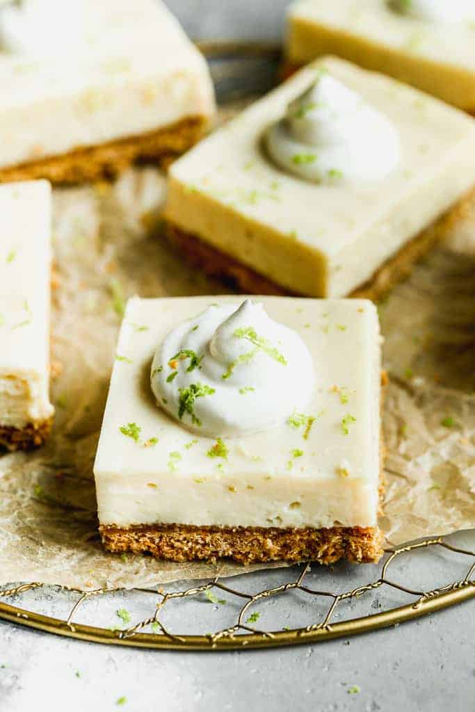 Key lime pie bars with whipped cream on top and garnished with lime zest.