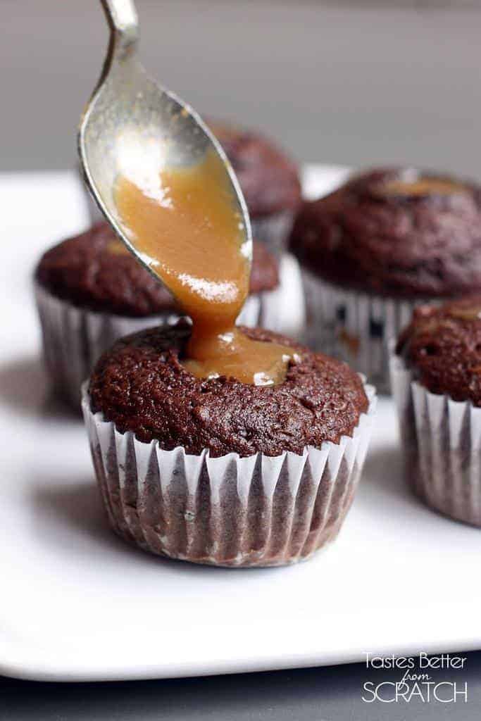 A spoon dripping caramel sauce into the center of a chocolate muffin.