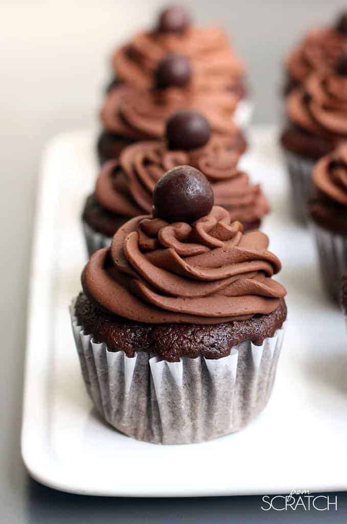 Many chocolate cupcakes topped with piped chocolate frosting and a chocolate candy on top.