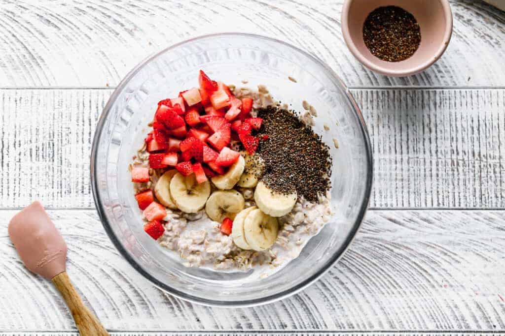 A mixture of oats, milk and yogurt in a bowl, topped with fresh strawberries, bananas and chia seeds.