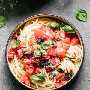 A bowl with cooked spaghetti topped with a fresh tomato basil sauce.