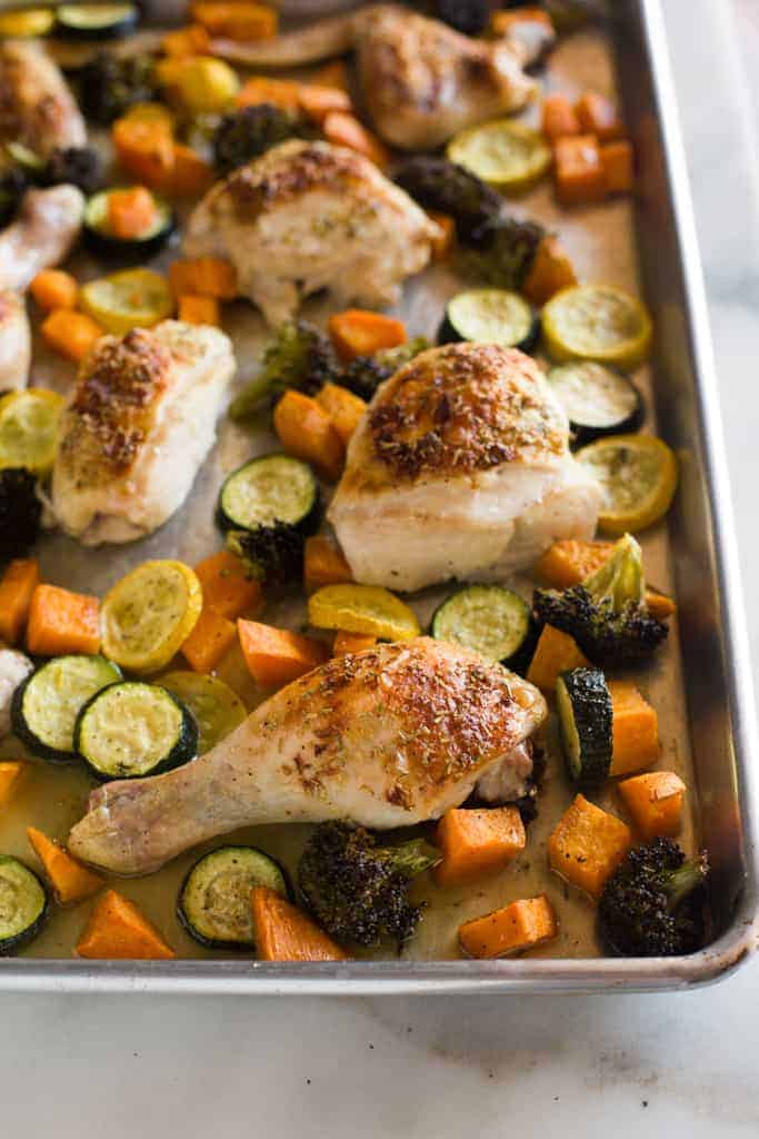A sheet pan with roasted chicken and vegetables including zucchini, sweet potato and broccoli. 