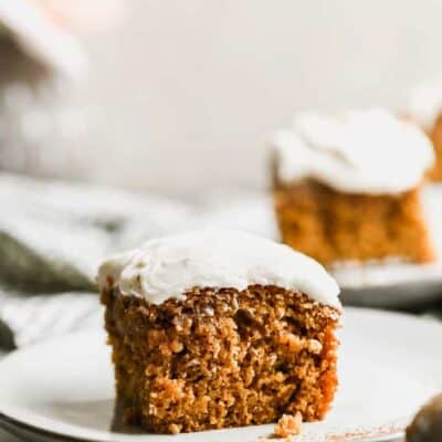 A slice of pumpkin cake with cream cheese frosting, on a plate.